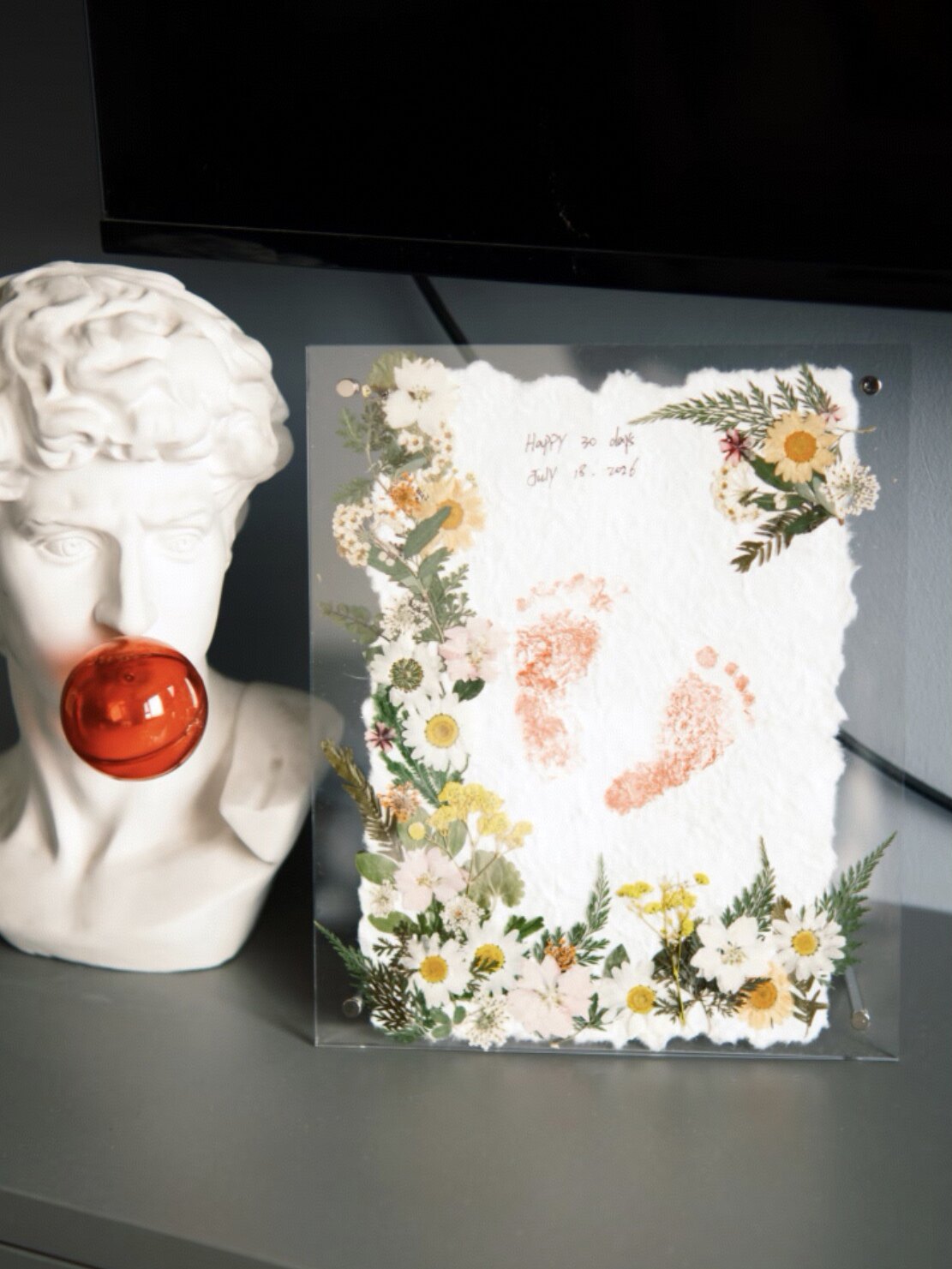 Framed keepsake combining a child's footprint with pressed flowers